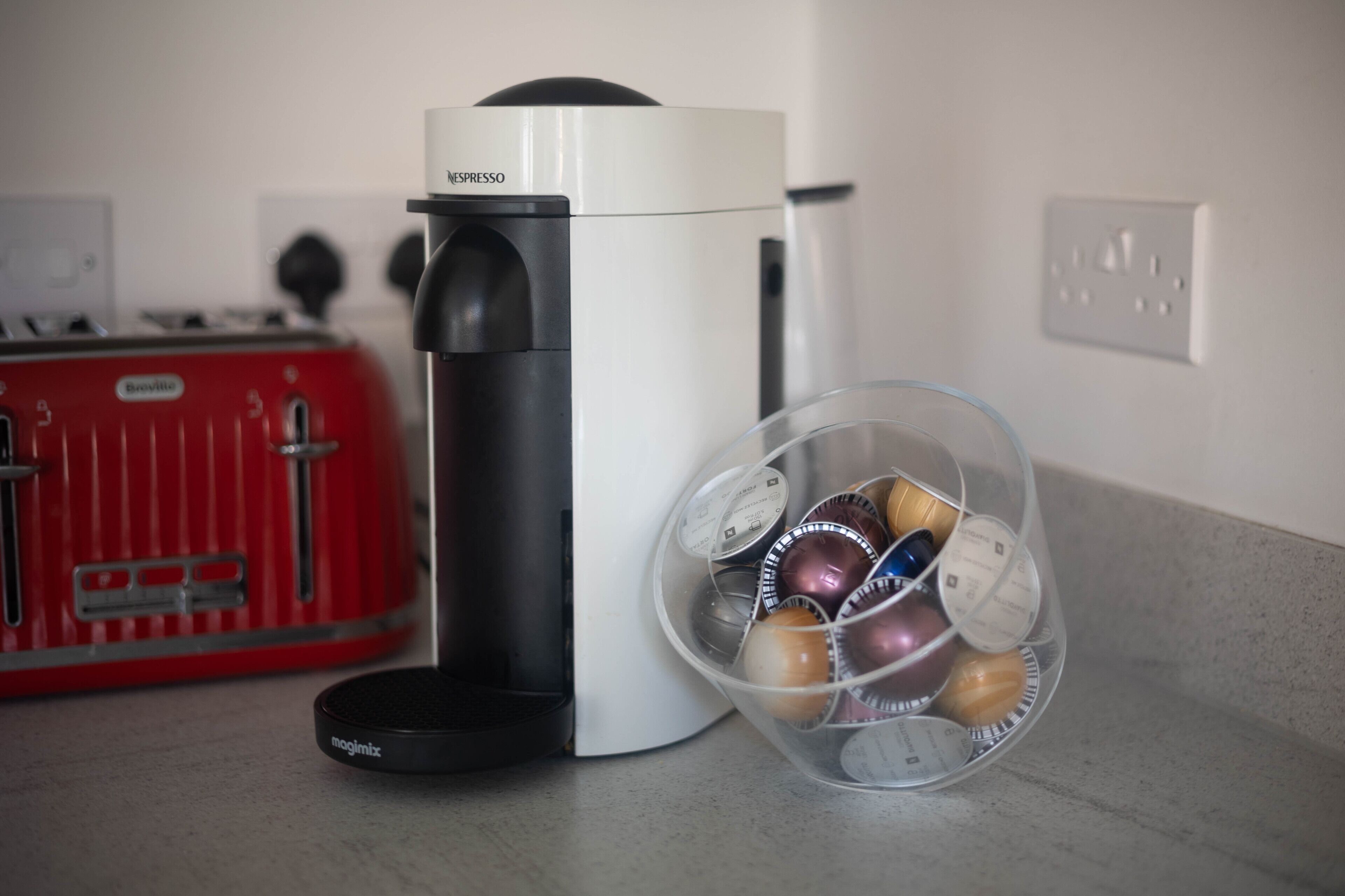 Eine Kaffeemaschine mit einem separaten, transparenten Behälter für Kaffeekapseln.