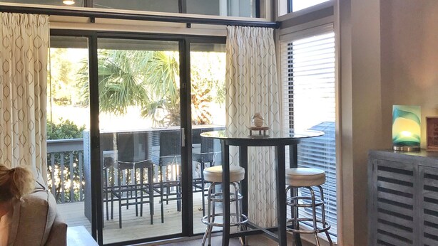 A spacious room with a ceiling fan, a dining table with chairs, a sofa, and a view of the outdoors through large sliding glass doors.
