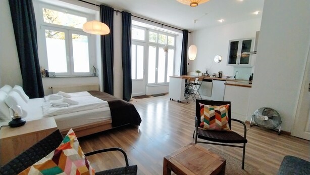 A modern hotel room with a bed, a desk, a chair, and a small table. There is a kitchenette in the background. - Great value in Prenzlauer Berg, free parking (Berlin)