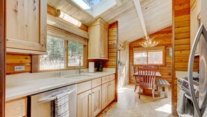 Une cuisine rustique aménagée dans une cabane en bois, avec un puits de lumière, des placards en bois, un évier, une table à manger avec des chaises et un réfrigérateur.