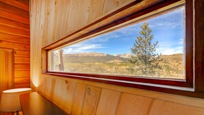 L'intérieur d'un chalet en bois, doté d'une grande fenêtre qui offre une vue sur un paysage montagneux.
