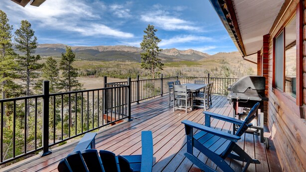 Une terrasse en bois avec une table et des chaises, un barbecue et une vue sur les montagnes.