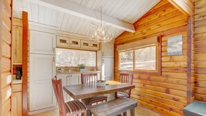 L’intérieur d’un chalet en bois comprend une table à manger, des chaises, un banc, un lustre et un réfrigérateur.