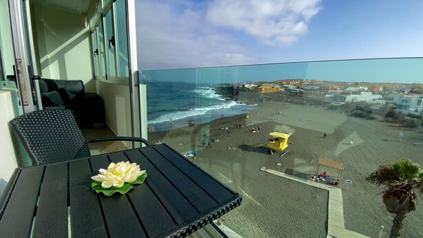 A balcony with a view of the beach, a table with a flower, and a lifeguard tower. - On the beach with unbeatable views  (Telde)