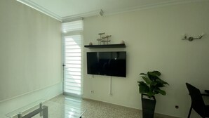 A modern living room with a flat-screen TV mounted on the wall, a potted plant, and a dining area with a glass table and chairs. - On the beach with unbeatable views  (Telde)