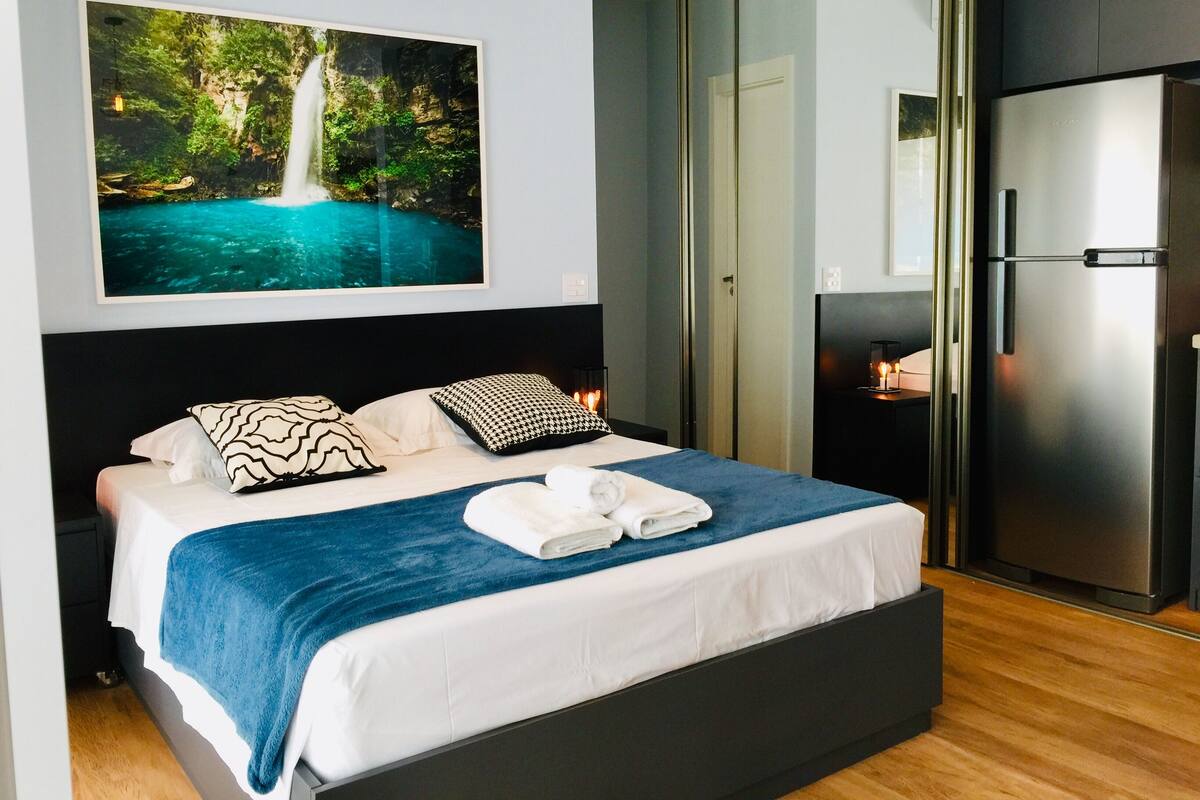 Un dormitorio moderno con una cama grande, un armario negro, un refrigerador y un cuadro con una cascada.