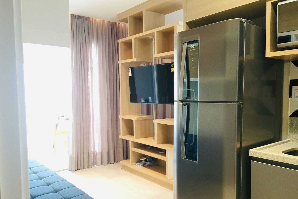 Una cocina moderna con refrigerador empotrado, repisas de madera y televisor de pantalla plana.