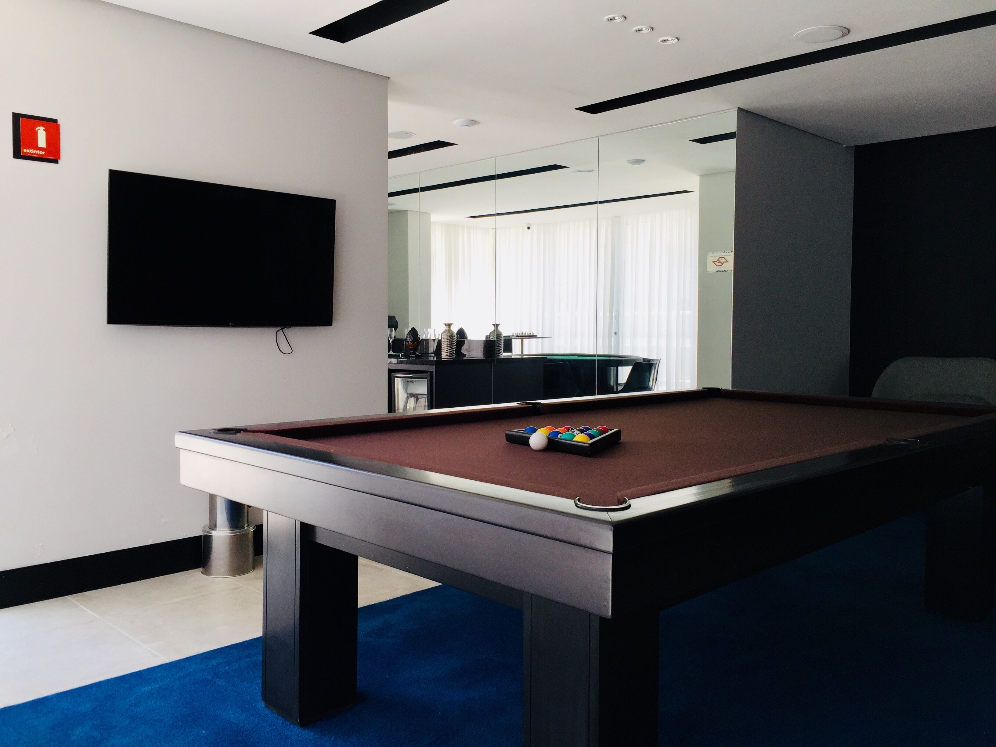 Una mesa de billar con bolas, un televisor en la pared y un letrero de extintor.