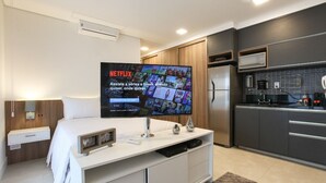 Una habitación de hotel moderna con una televisión de pantalla plana grande, una cama, una mesita de noche, un armario y una kitchenette.