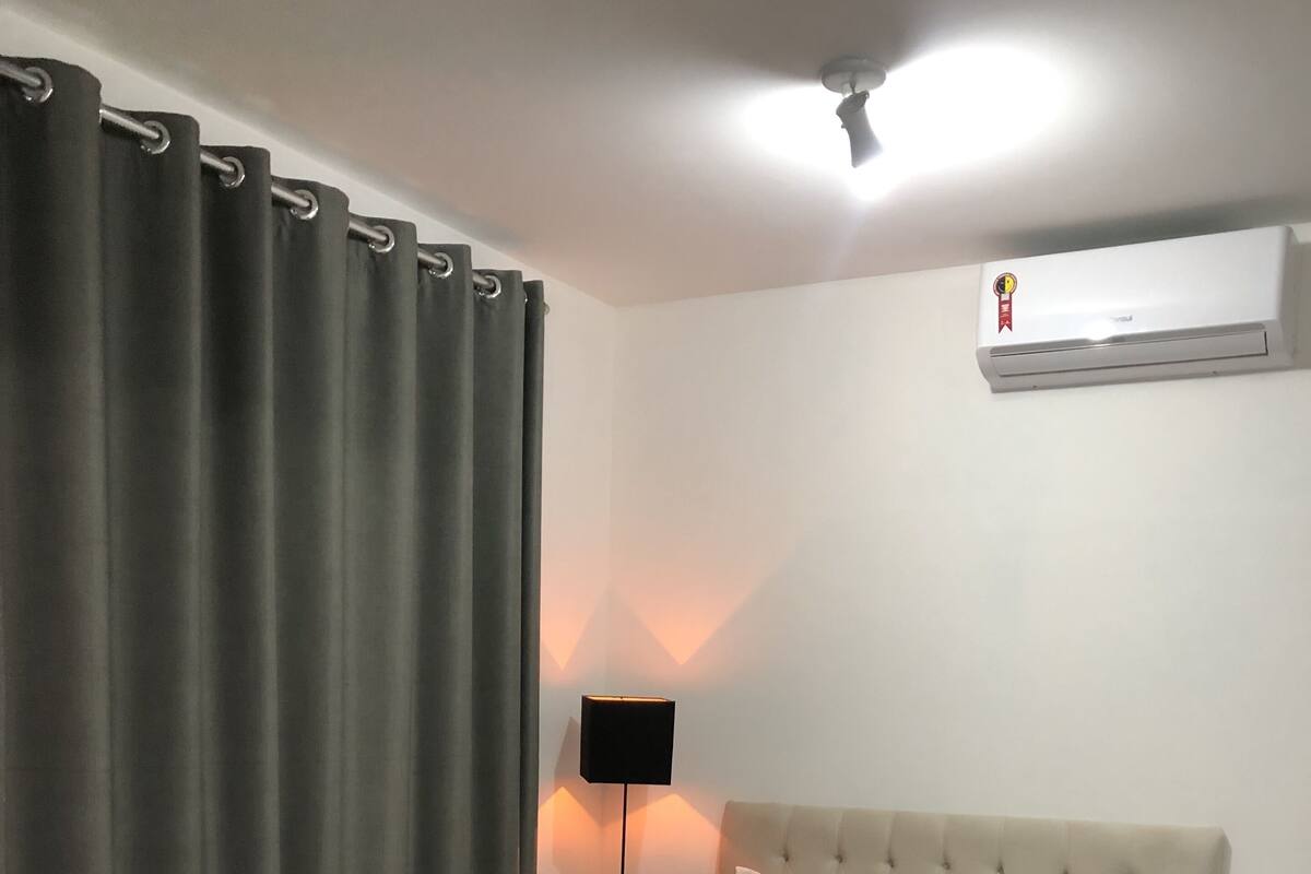 Un dormitorio con cama, cortinas, aire acondicionado montado en la pared y una lámpara de pie.
