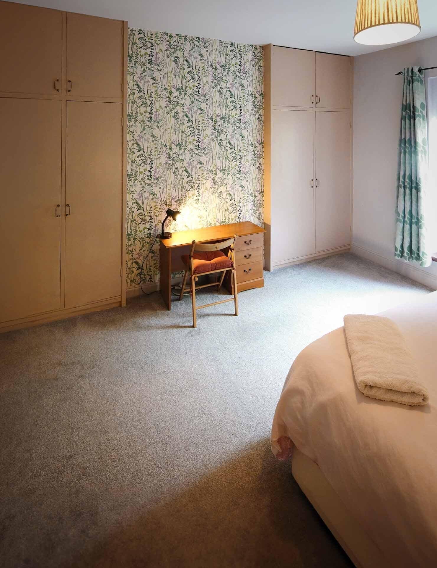 Et soveværelse med en seng, et skrivebord med stol og en garderobe.