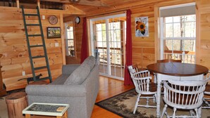 L’intérieur d’un chalet en bois comprend un canapé, une table à manger, des chaises, un ventilateur de plafond et une grande fenêtre.