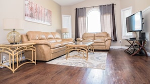 A living room with two leather sofas, a glass coffee table, a lamp, a TV, and a painting on the wall. - 3 Beds 2 Baths by Costco, GP Airport, Restaurants (Grande Prairie)