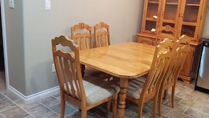 A dining area with a wooden table and six chairs, a wooden cabinet with glass doors, and a tiled floor. - 3 Beds 2 Baths by Costco, GP Airport, Restaurants (Grande Prairie)