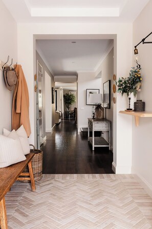 Un couloir avec un parquet en chevrons, un banc, un porte-manteau et une lampe fixée au mur.