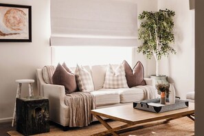 Een woonkamer met een bank, een salontafel, een plant en een schilderij aan de muur.