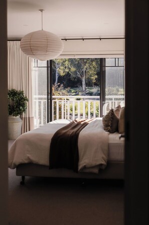 Une chambre avec un grand lit, un luminaire suspendu, une vue sur un balcon agrémenté de plantes et une plante en pot placée à côté du lit.
