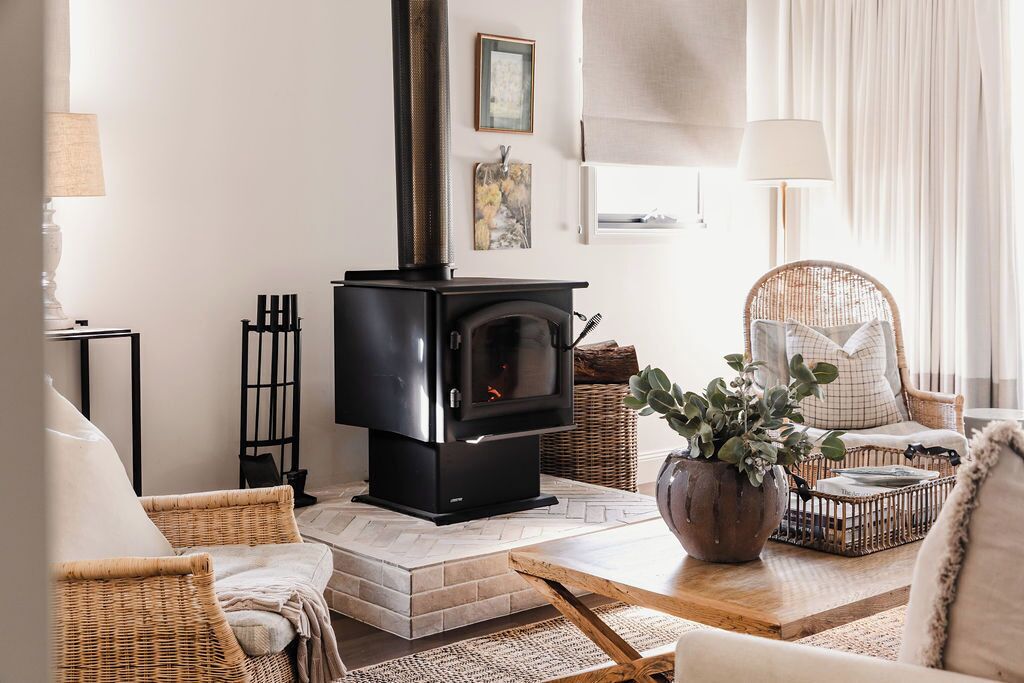 A cozy living room with a fireplace, wicker furniture, and a potted plant.