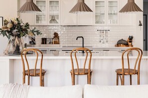 Une cuisine moderne avec des meubles blancs, un îlot central et trois chaises en osier.