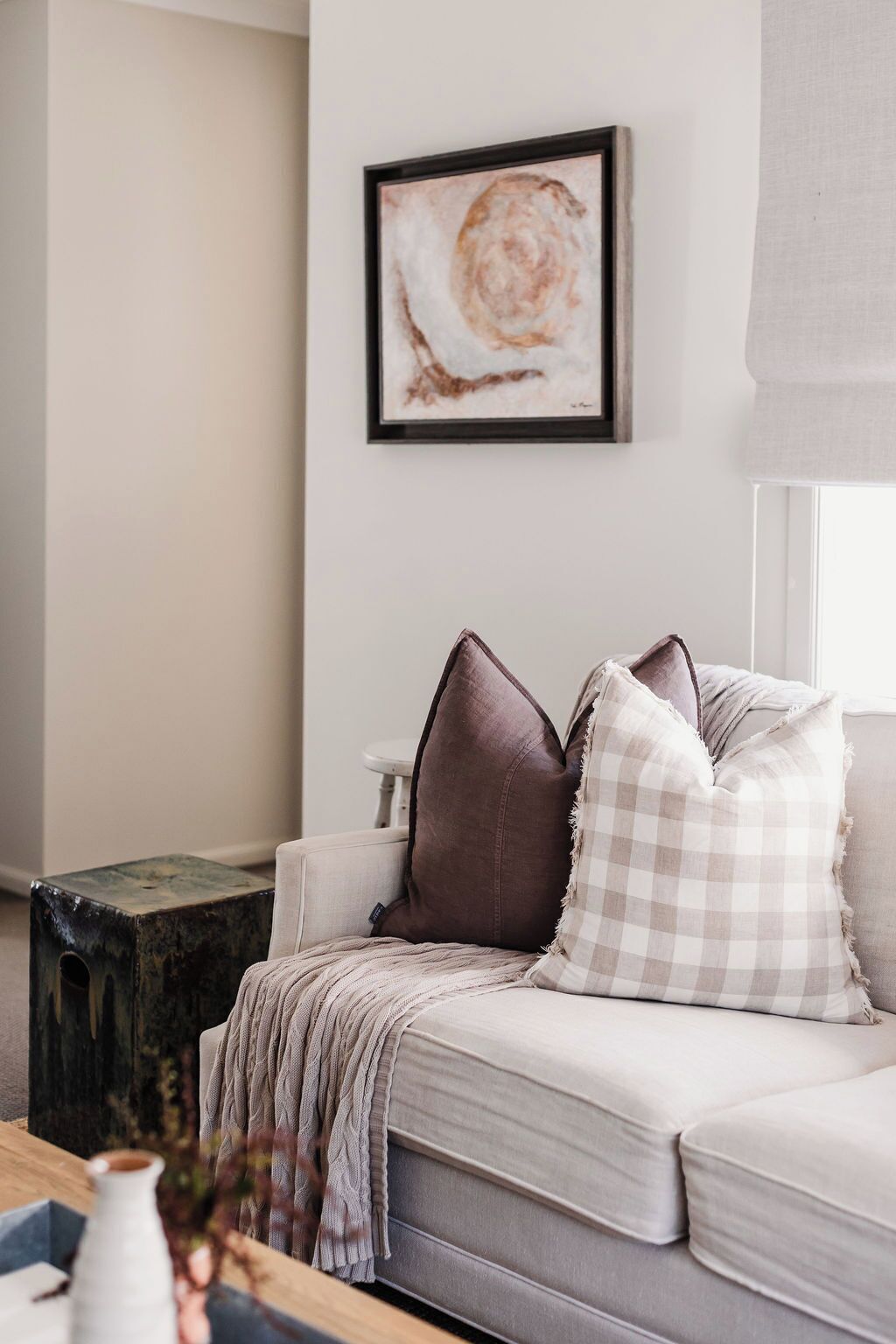 A modern living room with a sofa, cushions, a framed artwork, and a window with blinds.