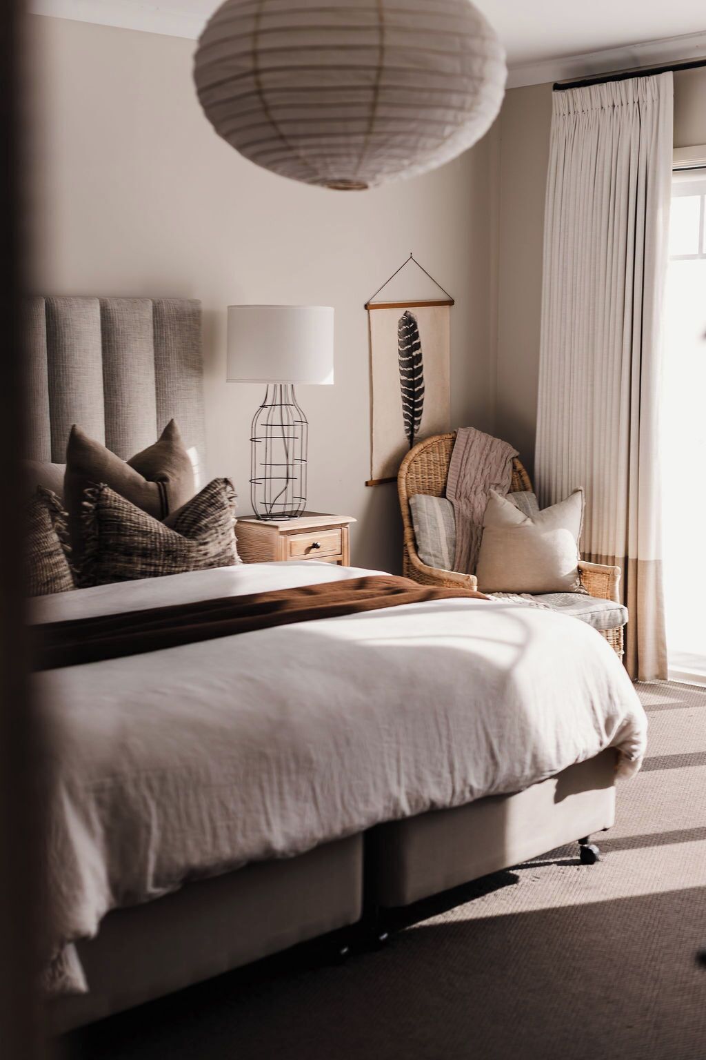 A bedroom with a bed, bedside tables, a lamp, a wall hanging, and a window with curtains.