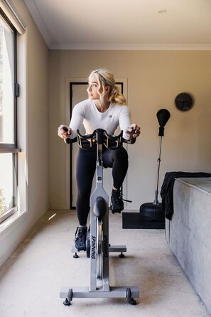 A person using a stationary bike in a room with a large window, a door, and a wall-mounted clock.