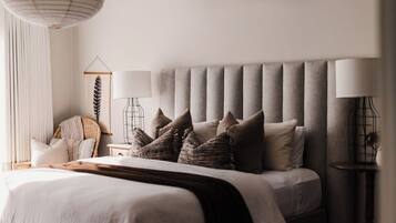 A bedroom with a large bed, a bedside table, a lamp, and a wall-mounted shelf.