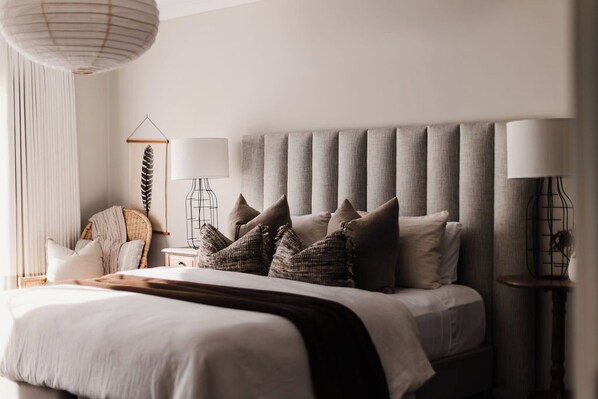 A bedroom with a large bed, a bedside table, a lamp, and a wall-mounted shelf.