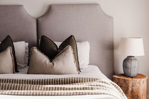 Een bed met hoofdbord, kussens, een bedlampje en een houten nachtkastje.