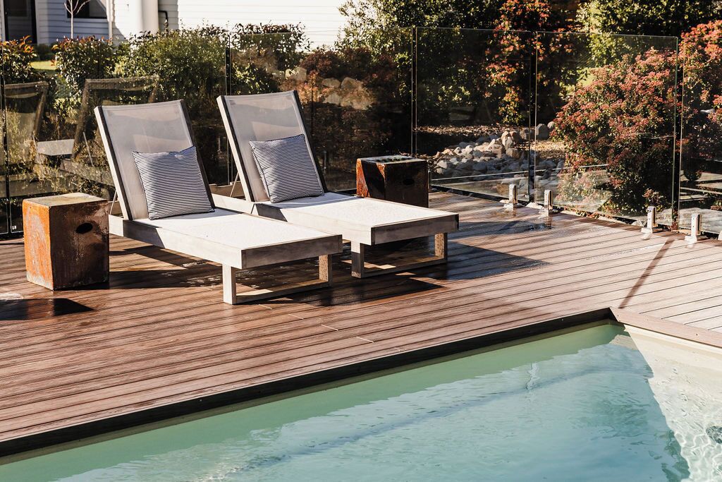 A poolside area with two lounge chairs and a small table, surrounded by a wooden deck.