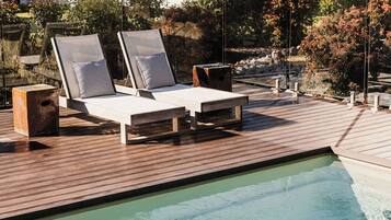 A poolside area with two lounge chairs and a small table, surrounded by a wooden deck.