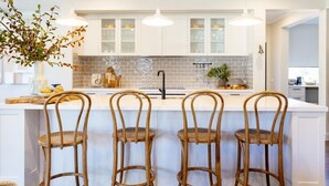 Une cuisine moderne avec des meubles blancs, un îlot central doté de tabourets et des luminaires suspendus.