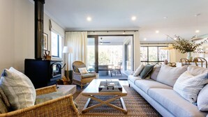 Un salon chaleureux avec une cheminée, des meubles en osier, un canapé et une vue sur l’extérieur, accessible par une porte vitrée.