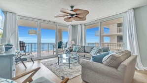 Een ruime woonkamer met een grote glazen deur die leidt naar een balkon met uitzicht op het strand.