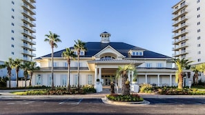 A hotel with a central entrance, surrounded by palm trees and a parking lot. - Avalon 810 | Beachfront | Amazing Views | Wrap Around Balcony | Resort Amenities (Gulf Shores)