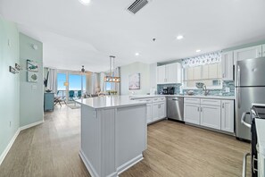 A modern kitchen with white cabinetry, a central island, and a dining area with a view. - Avalon 810 | Beachfront | Amazing Views | Wrap Around Balcony | Resort Amenities (Gulf Shores)