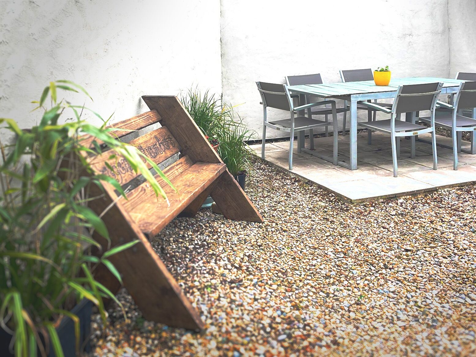A patio area with a wooden bench, a table with chairs, and a yellow pot on the table.