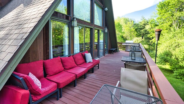 Une terrasse en bois avec un canapé rouge et une table en métal, offrant une vue sur un paysage verdoyant luxuriant.