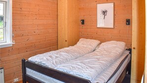 En enkeltseng i et træværelse med et vindue og en lampe monteret på væggen.