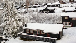 En snedækket landsby med træhuse, et markant træ og en bygning med en rød dør.