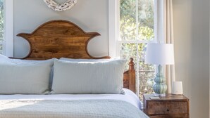 A bedroom with a wooden headboard, a white bedspread, and a bedside table with a lamp and a vase.