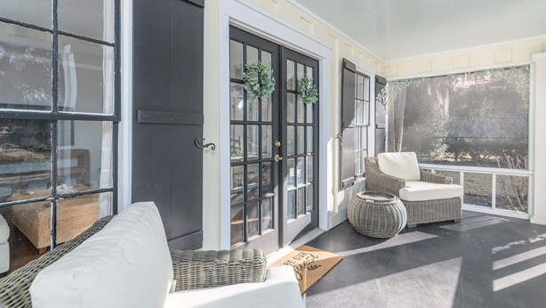 A covered porch with a white sofa, wicker chairs, and a wicker basket.