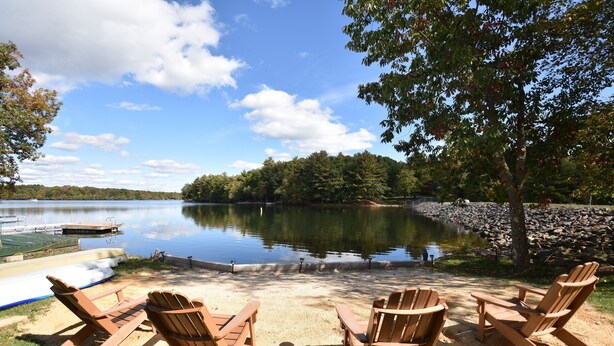 A lakeside view with four Adirondack chairs facing a calm lake, surrounded by trees and a dock. - Lake front with Private Beach, Hot tub, Pool, Pickle Ball, March Dates available (Jim Thorpe)