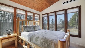A wooden bed with a headboard, a bedside table, and a window with a view of trees. - Lake front with Private Beach, Hot tub, Pool, Pickle Ball, March Dates available (Jim Thorpe)