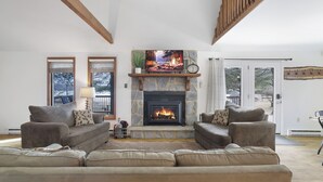A living room with a stone fireplace, two sofas, a television, and a large window. - Lake front with Private Beach, Hot tub, Pool, Pickle Ball, March Dates available (Jim Thorpe)
