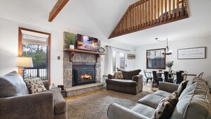 A living room with a fireplace, sofas, a dining area, and a staircase. - Lake front with Private Beach, Hot tub, Pool, Pickle Ball, March Dates available (Jim Thorpe)