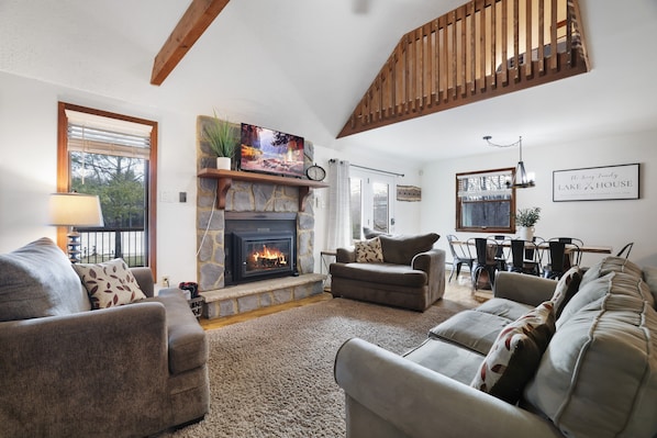 A living room with a fireplace, sofas, a dining area, and a staircase.