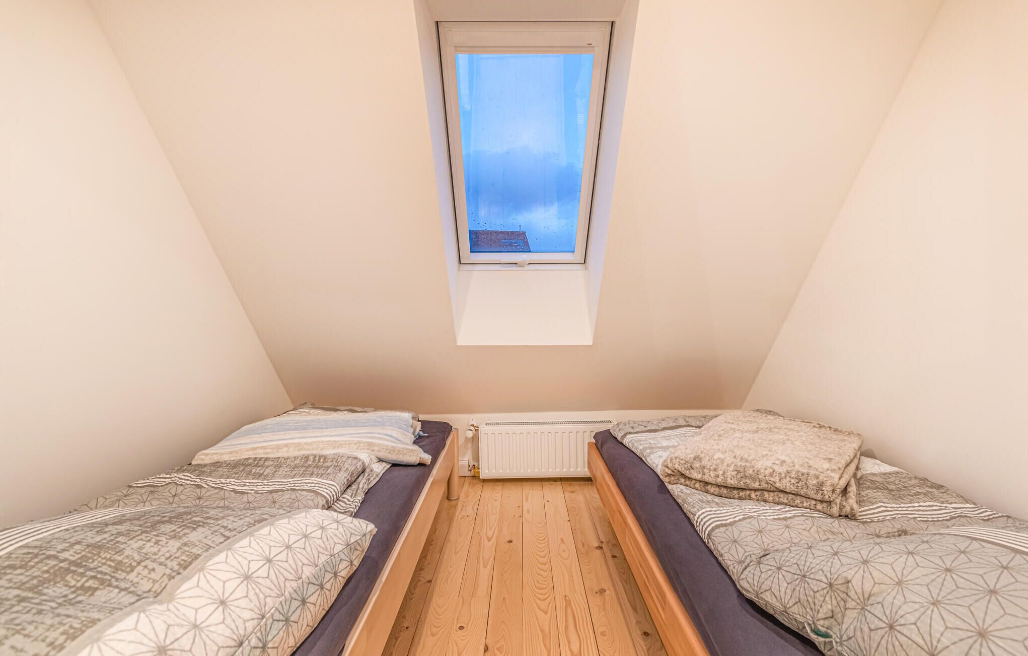 A small, cozy room with two beds, a wooden floor, and a window overlooking a building.