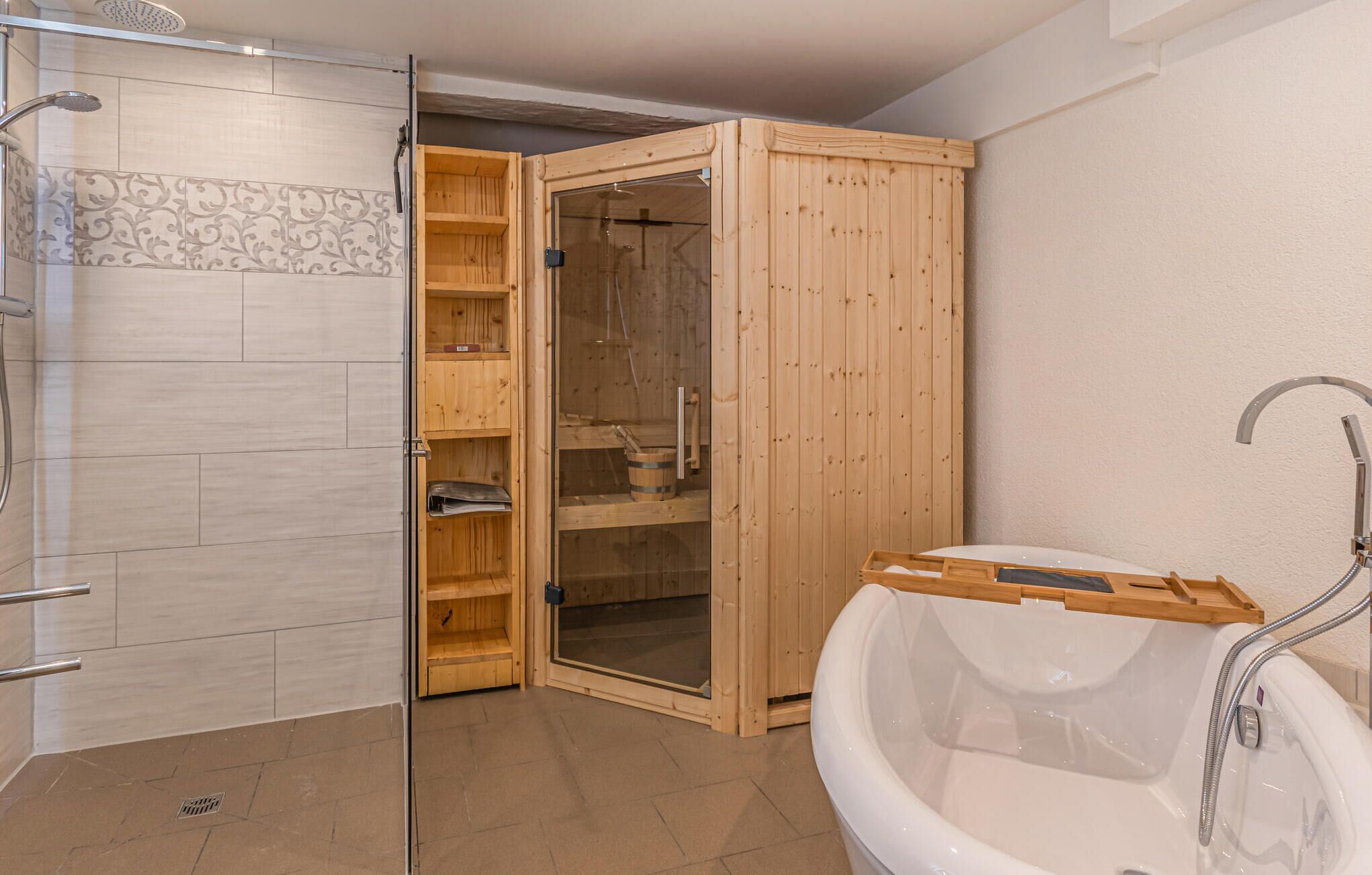 A bathroom with a wooden shower enclosure, a glass shower door, a white bathtub, and a wooden shelf unit with storage.