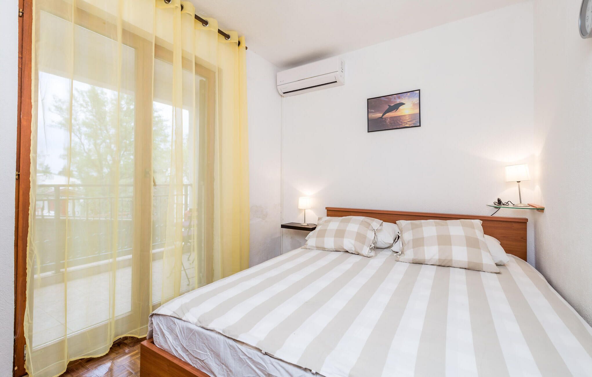 Un dormitorio con cama, ventana con cortinas, aire acondicionado, lámpara de pared y un cuadro enmarcado.